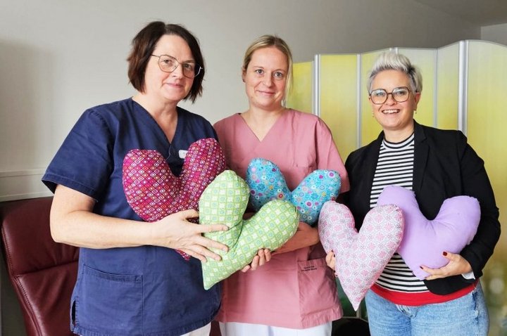 Drei Frauen halten große bunte Herzkissen für Brustkebspatientinnen in den Händen