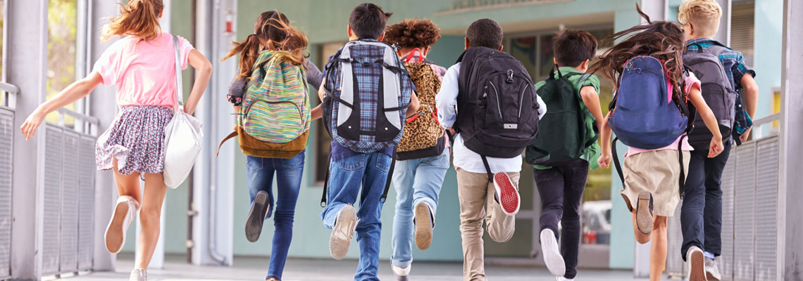 Schulkinder mit Ranzen laufen im Schulflur, Ansicht von hinten